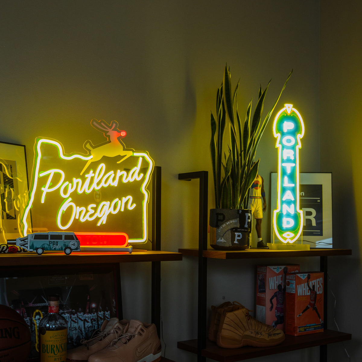 A brightly lit room features shelves displaying various items and neon signs. An LED Marquee Sign outlines the shape of Oregon and reads "Portland Oregon" in yellow and red, while another vertical custom LED sign displays "Portland" in teal and white. Decorative items and plants are also visible, enhancing the energy-efficient ambiance.